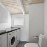 Washroom with washing machine, sink, and toilet under wooden ceiling.