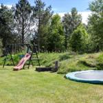Backyard with trampoline, playground, and lawn.