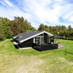 Black wooden house with terrace and garden. Surrounded by trees under blue sky.