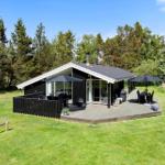 Modern wooden cabin with large deck, grill, and seating areas in the green.