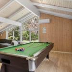 Pool table with balls and cue in a room with wooden wall and large window.