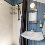 Bathroom with shower, sink, and mirror on blue wood panel wall.