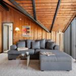 Living room with gray sofa, wooden walls, and sloped ceiling