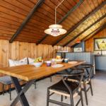 Dining area with wooden table, chairs, and kitchen under wooden ceiling.