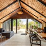 Living and dining area with wooden ceiling, table, and sofa. Passage to terrace with garden view.