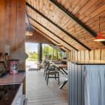 Kitchen with dining area under wooden ceiling, table, chairs, and window view.