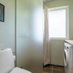 Bathroom with toilet, washing machine, and window with curtain.
