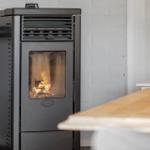 Ravelli wood stove with burning fire in modern kitchen with white brick wall.