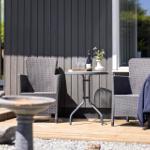 Outdoor area with two chairs, table, and wine bottle against gray siding.