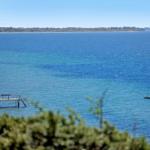 Sea view with pier and small boat in the water. Holiday home directly on the shore.