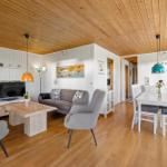 Living and dining area with hardwood floor, white wall paneling, and wood ceiling. Furniture in gray and white.