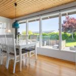 Dining room with white table, chairs, and large window view of garden.