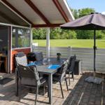 Patio with table, chairs, and umbrella. Background: green field and wooden fence.