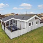 Ein Ferienhaus mit Terrasse und Garten. Im Hintergrund sind Hügel und andere Häuser sichtbar.