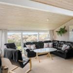 Wohnzimmer mit schwarzer Ledercouch, Holztisch und Blick auf die Landschaft.