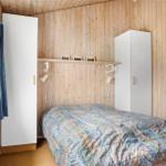 Schlafzimmer mit Holzwand, Bett, weißen Schränken und Fenster mit Vorhang.