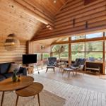 Wohnzimmer mit Holzwand, Sofa, Fernseher und Sitzgelegenheiten. Große Fenster mit Blick nach draußen.