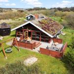 Holzhütte mit begrüntem Dach, Terrasse und Schaukel im Grün.
