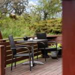 Terrasse mit Tisch, zwei Stühlen und Pflanzen. Hintergrund: Grünflächen und Bäume.