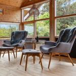 Zwei graue Sessel mit Felldecken stehen um einen runden Tisch herum. Holzfußboden und große Fenster.