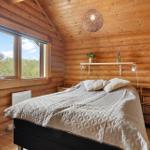 Schlafzimmer mit Holzwand, Bett, Fenster und Wandleuchten.