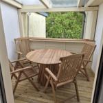 Terrasse mit runden Tisch und vier Holzstühlen, Blick auf grüne Bäume.