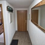 Flur mit Holztür, Spiegel und Blick in das Badezimmer mit Waschtisch.