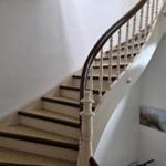 Eine Treppe mit weißer Balustrade und dunklem Geländer führt nach oben.
