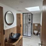 Bad mit Dusche, Waschbecken und Toilette. Holz und Steinoptik.