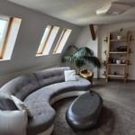 Wohnzimmer mit halbrundem Sofa, Dachfenstern und Holzregal.
