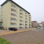 Five-story residential building with balconies and parking lot.