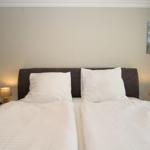 Two beds with white bedding, nightstands with lamps, and wall picture with lighthouse.