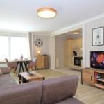 Living room with sofa, TV, and kitchen area in the background.