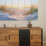 Cabinet with wooden top and black drawers. Wall picture shows beach at sunset.