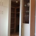 Glasvitrine mit Geschirr und Gläsern neben einem Kleiderschrank mit offenen Türen.