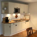Küche mit weißen Schränken, Herd, Spüle und Mikrowelle. Holztisch und Stuhl sind sichtbar.