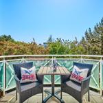 Balcony with two chairs, table, and view of greenery and sky.