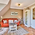 Wohnzimmer mit rotem Sofa, weißen Kissen und Holztisch. Tür führt zur Treppe.