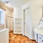 Badezimmer mit Dusche, Waschbecken und Fenster mit Blumen.