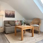 Wohnbereich mit Sofa, Rattan-Stuhl und Holztisch unter Dachschrägen.