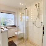 Badezimmer mit Dusche, Toilette und Fenster mit Blick auf Garten.