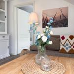 Ein Wohnzimmer mit Sofa, Tisch und Blumenarrangement. Wandbild und weiße Einbauschränke sind sichtbar.