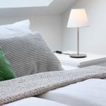 Doppelbett mit grünem und grauem Kissen, weißem Nachttisch und Lampe.
