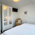 Schlafzimmer mit Bett, Kleiderschrank, Sessel und Wandbild.