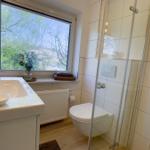 Badezimmer mit Dusche, Waschbecken und Fensterblick auf Grün.