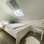 Ein Schlafzimmer mit Dachfenster, weißem Bett und Stuhl.