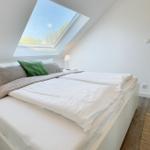 Schlafzimmer mit Dachschräge, großem Fenster und weißem Bett mit Kissen.
