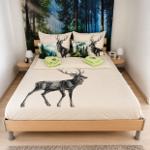 Schlafzimmer mit Bett, Wandbild Wald und Kissen mit Hirschmotiv.