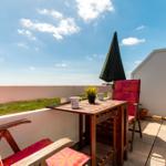 Terrasse mit Tisch, zwei Stühlen, Sonnenschirm und Blick auf Grünland.