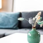 Ein grüner Vasen mit Trockenblumen steht auf einem Tisch vor einem Sofa.